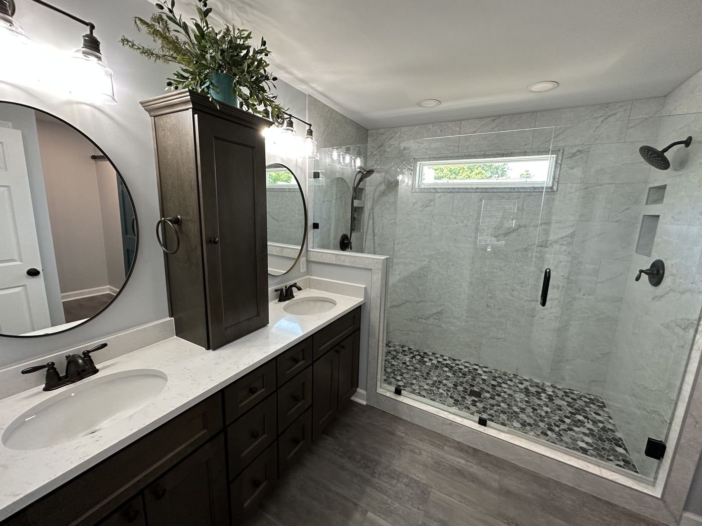 Glass-enclosed shower with a dark double vanity and round mirrors — Triangle Home Handyman, Apex NC
