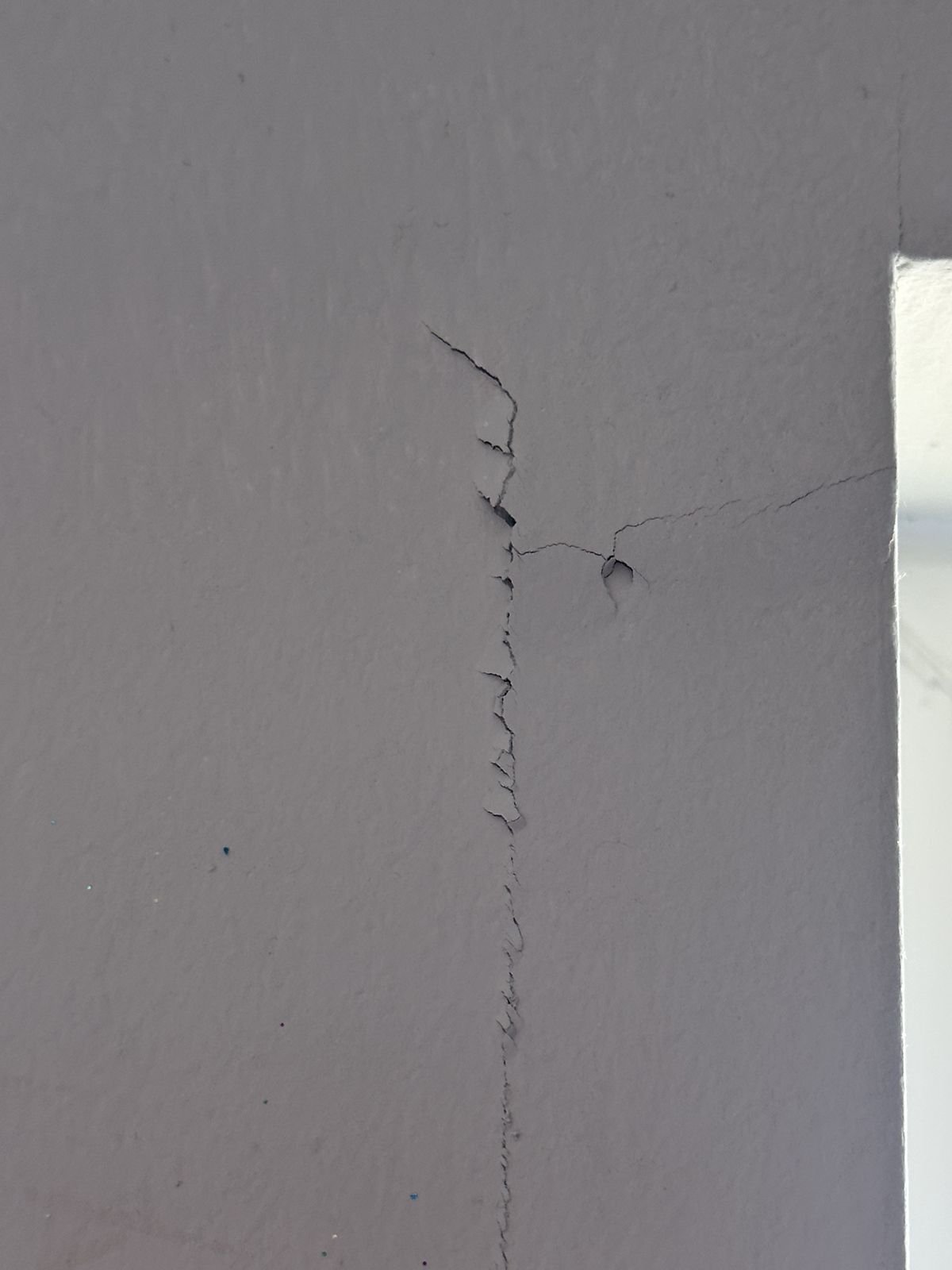 Cracked and peeling paint on the wall beside a window before repair