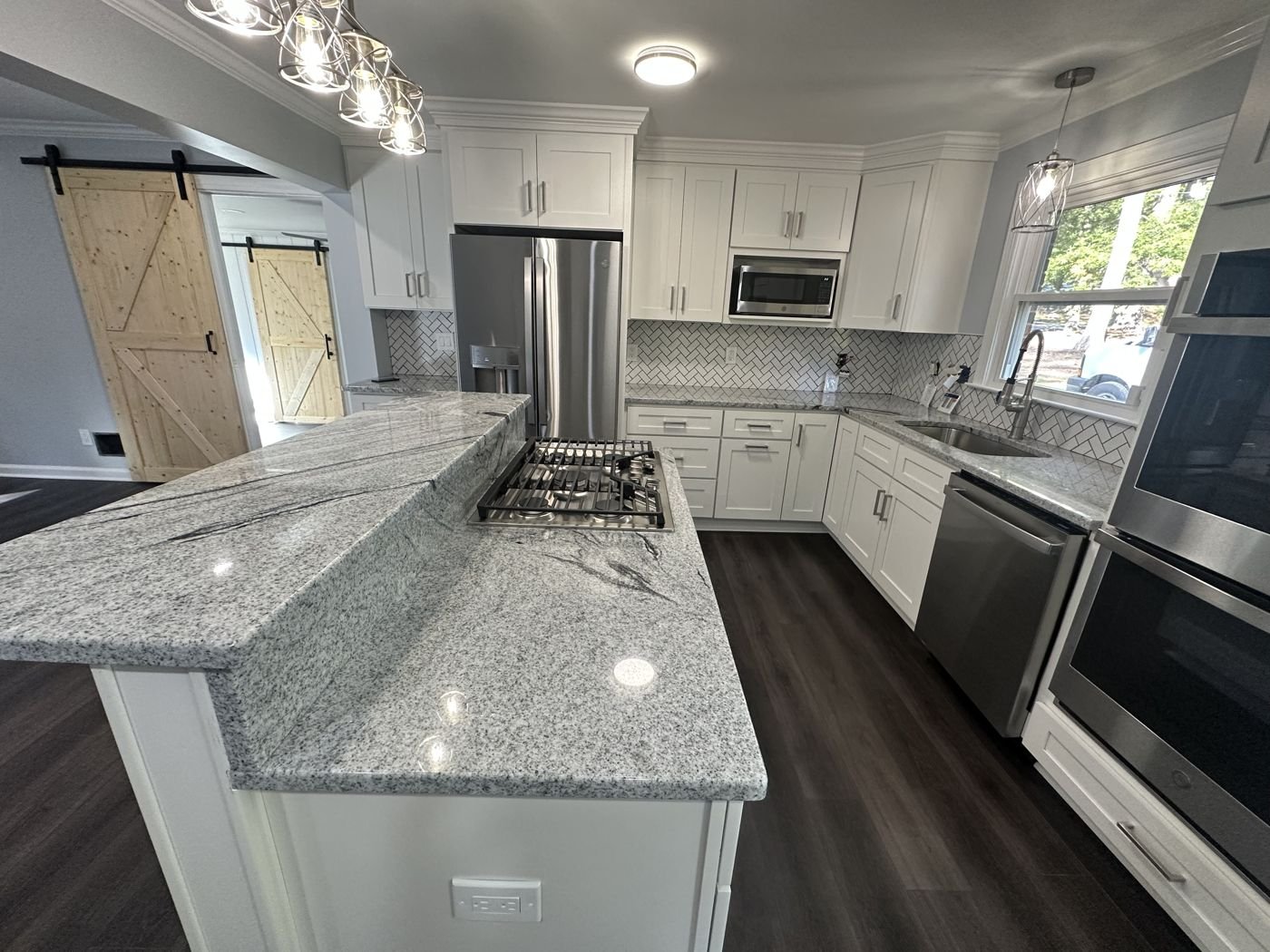 Two-level granite island with a gas cooktop, white shaker cabinets and herringbone backsplash — Triangle Home Handyman, Apex NC